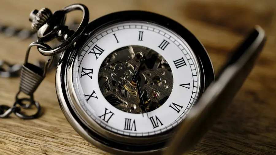 Person holding an open-face pocket watch, examining the visible dial with natural lighting