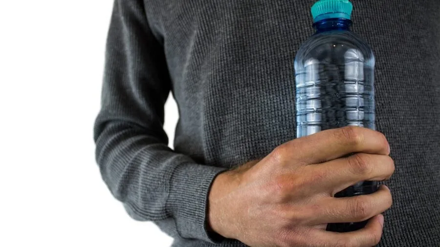 Person holding and drinking from a reusable water bottle during outdoor activity