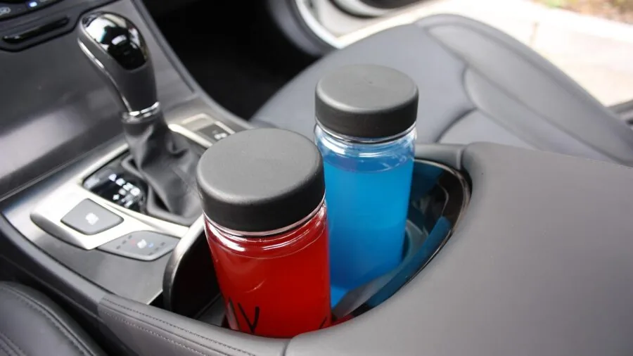 Person holding beverage in vehicle cup holder during drive