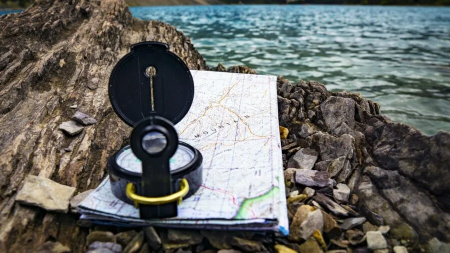 Person holding compass while hiking through mountainous terrain to navigate direction