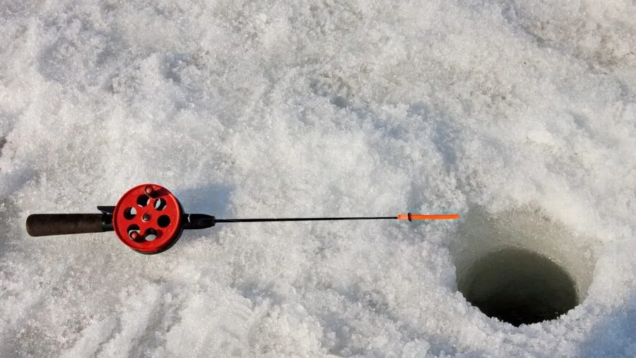 Person ice fishing on frozen lake holding fiberglass rod in winter conditions