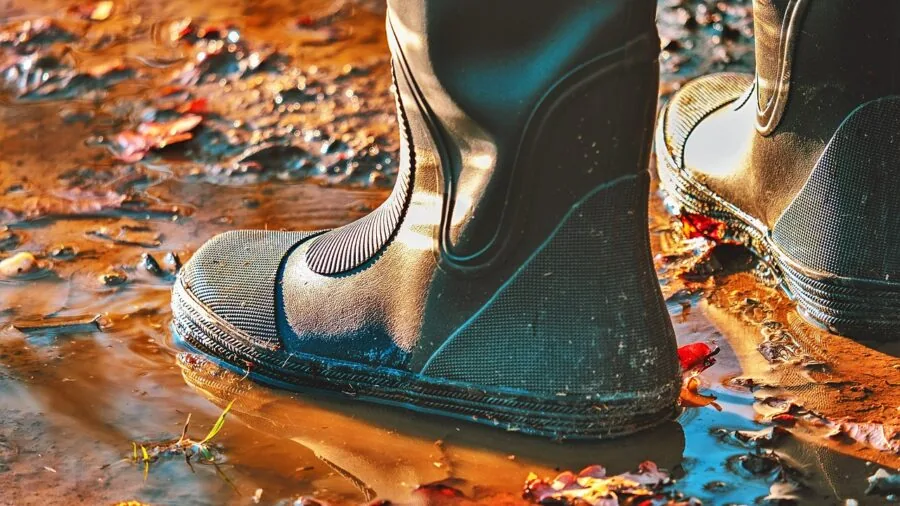 Person in rain boots standing in puddle during rainy weather outdoors
