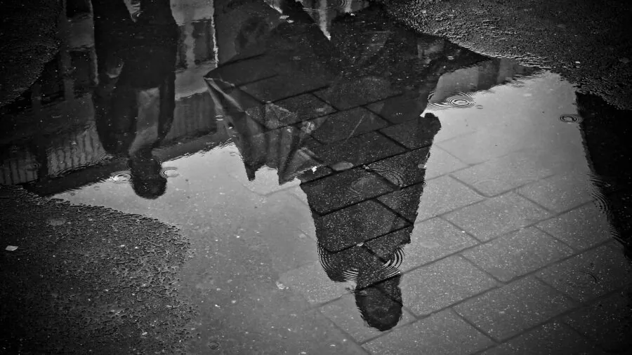 Person in rain boots stepping through puddles on wet street during rainfall