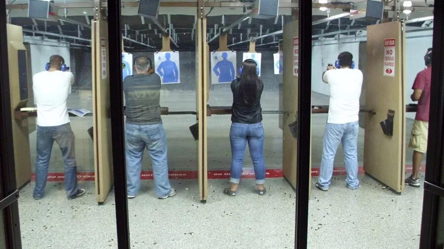 Person in shooting stance with rifle at outdoor range, demonstrating proper form and gear compatibility