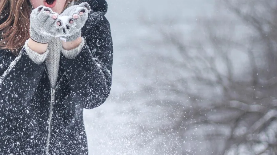 Person in winter clothing wearing warm gloves while enjoying outdoor cold weather activity