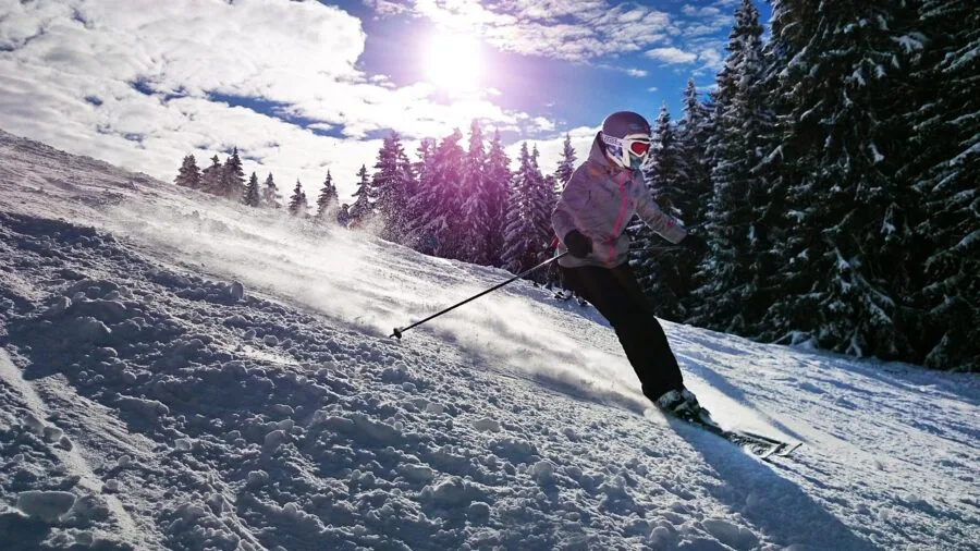 Person in winter gear adjusting ski helmet strap with gloved hands on snowy slope