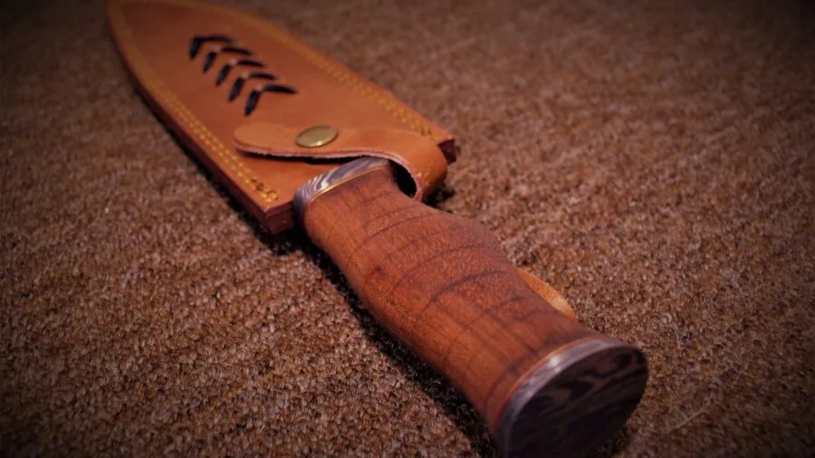 Person inspecting a hunting knife while standing in natural wilderness setting, evaluating quality and craftsmanship