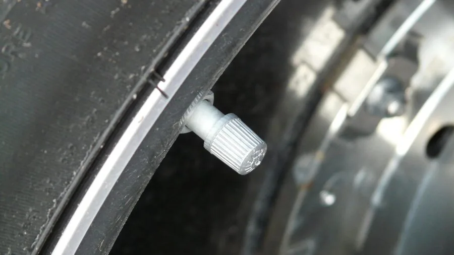 Person inspecting vehicle tire valve stem during routine car maintenance outdoors
