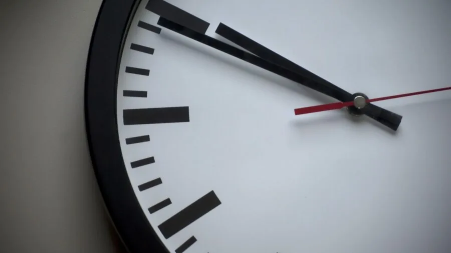 Person installing a wall clock on home interior wall with hammer and nail