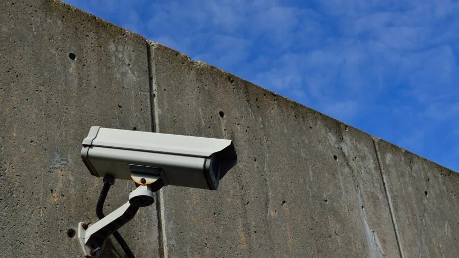 Person installing a wired security camera on exterior home wall for surveillance system