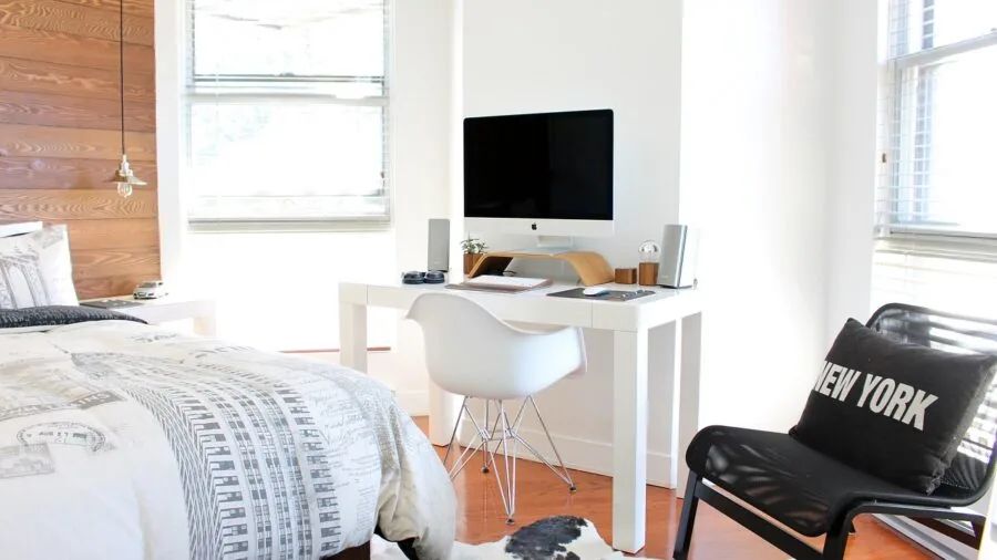 Person installing bed skirt under mattress on platform bed in bright bedroom