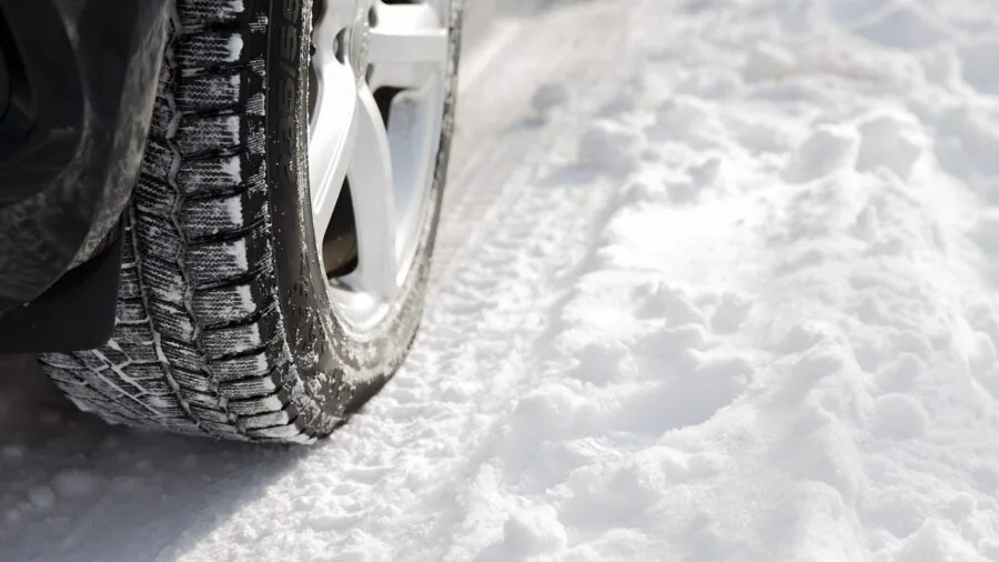 Person installing winter tires on vehicle in snowy conditions for seasonal vehicle preparation