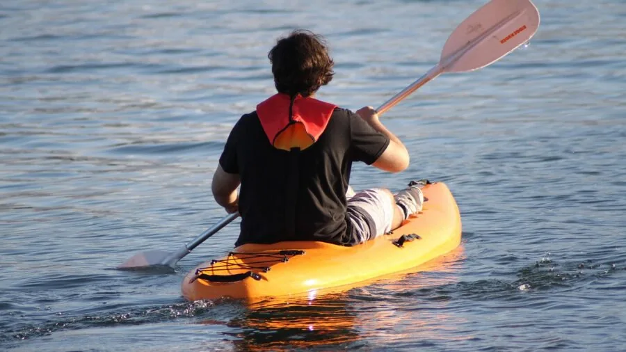 Person kayaking on peaceful water, showing the physical effort and technique of paddling during a long day on the water