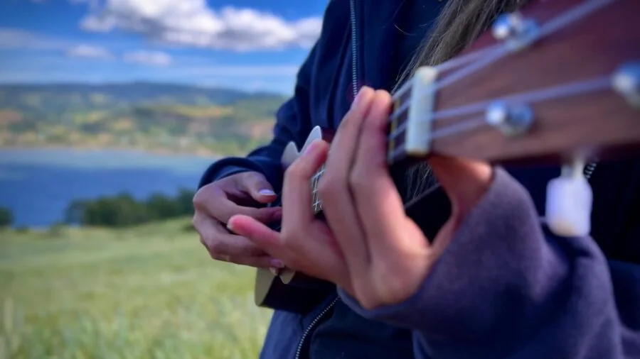 Person learning to play ukulele with various accessories and instructional materials in a home setting