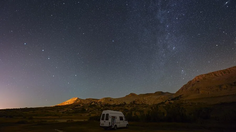 Person loading camping gear and tent into vehicle trunk for road trip adventure