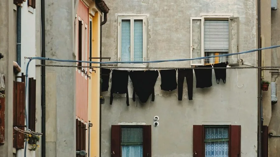 Person loading clean clothes into washing machine at home laundry room