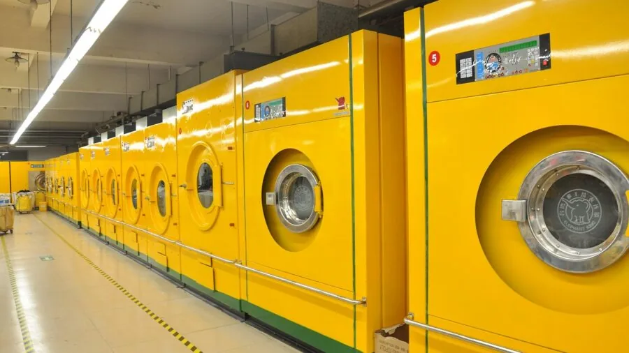 Person loading fresh white bedding into washing machine for cleaning and maintenance