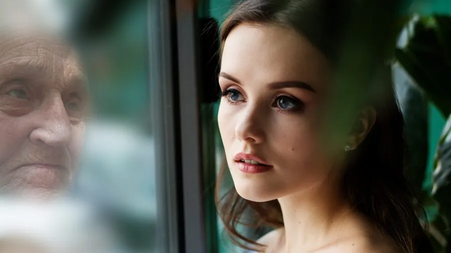 Person looking at their skin in mirror, examining a blemish on their face in natural light