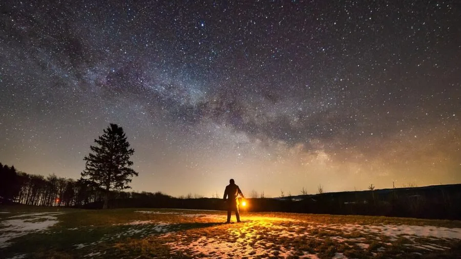 Person looking out at dark nighttime landscape with distant lights visible