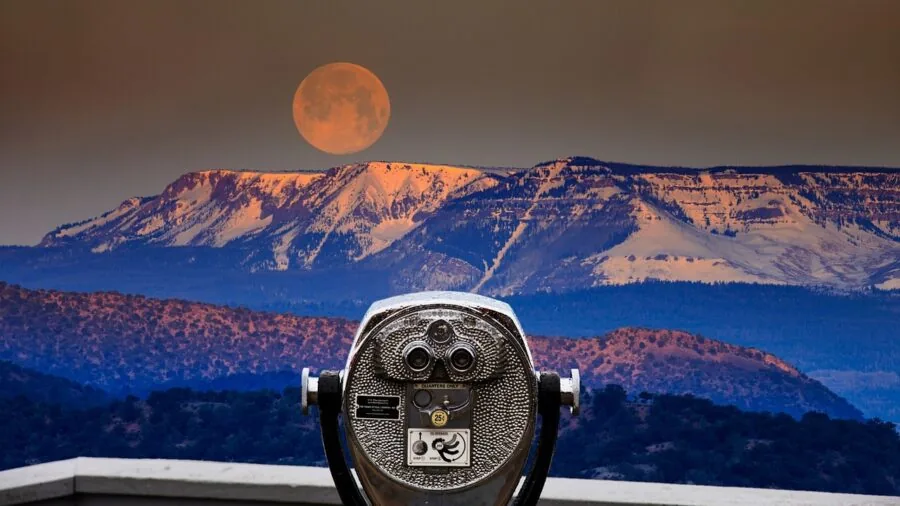 Person looking through spotting scope at distant mountain landscape during daytime outdoor activity