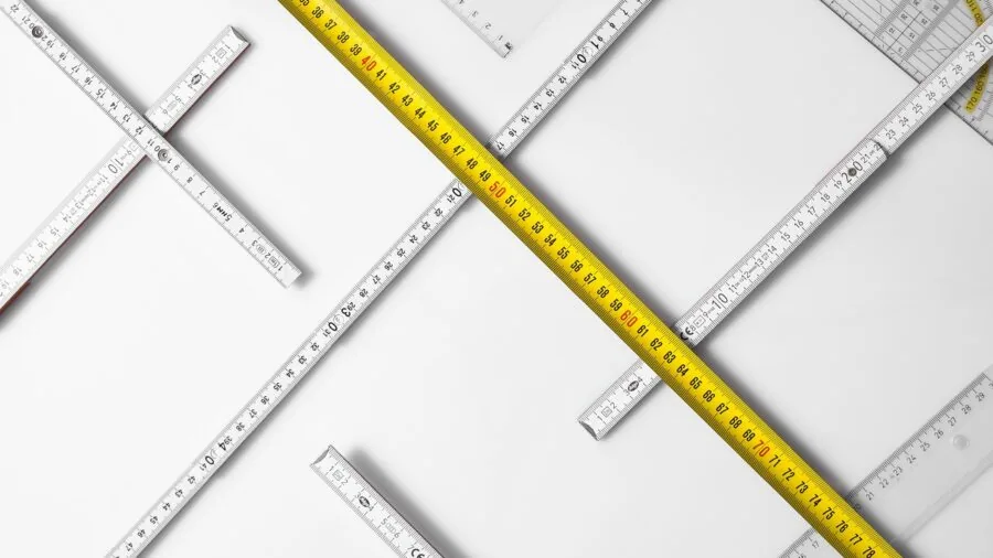 Person measuring backyard space with tape measure for outdoor storage planning