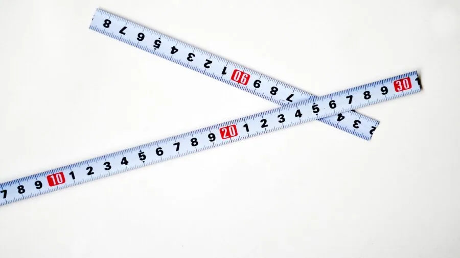 Person measuring bookshelf height and width with tape measure for proper sizing and placement planning