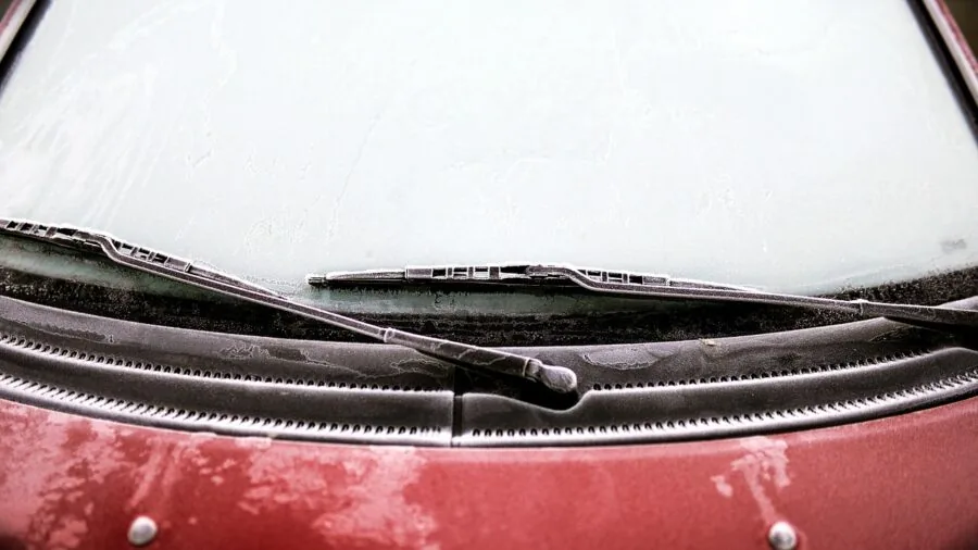 Person measuring car windshield width in snowy winter conditions for proper snow cover fit