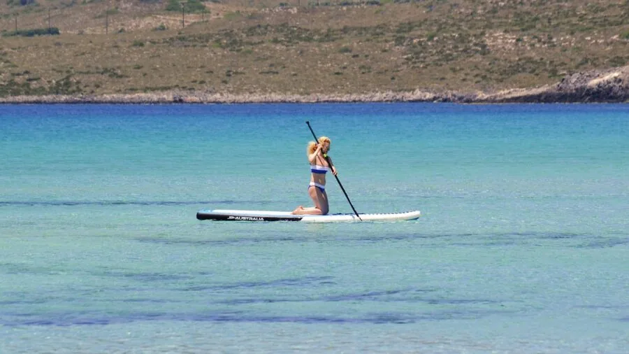 Person measuring inflatable paddleboard length and width specifications in shallow water