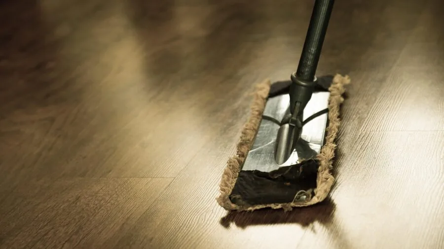 Person mopping hardwood floor with bucket during home cleaning routine