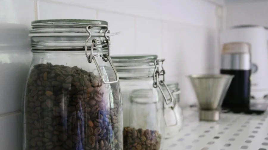 Person opening a glass storage jar in a bright kitchen, demonstrating proper lid seal and container handling