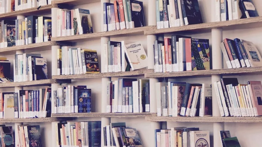 Person organizing books on wooden shelves in a well-lit home library space