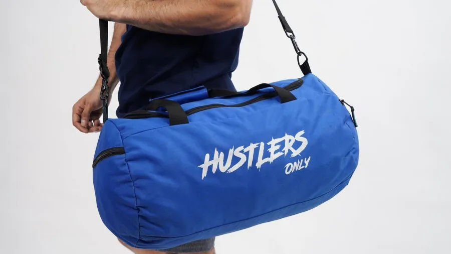 Person organizing clothes into a travel duffel bag on a bed, preparing for a weekend trip