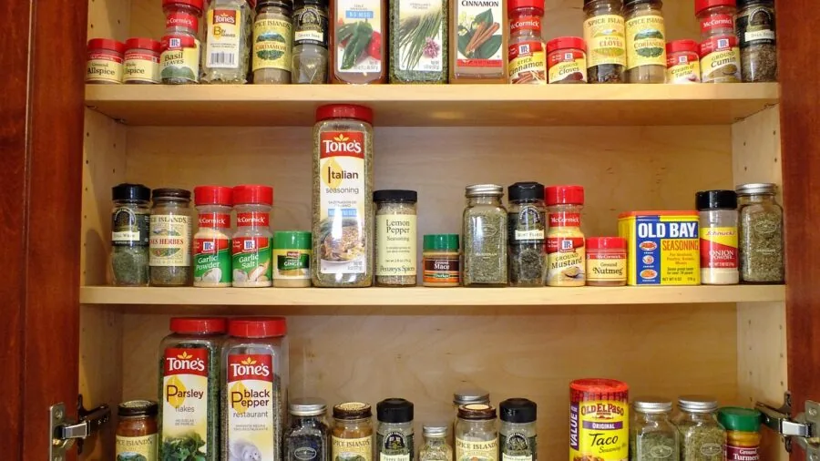 Person organizing glass containers in a bright kitchen pantry, planning food storage solutions