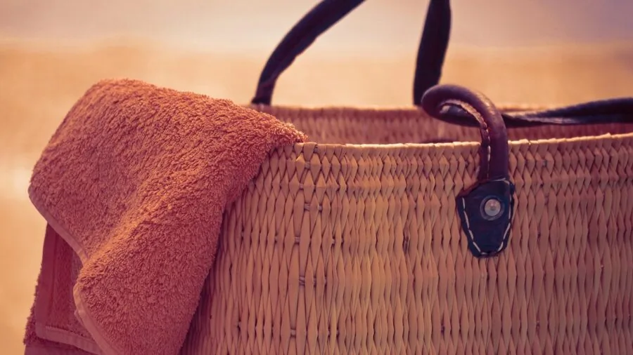 Person organizing wet and dry items in beach bag at sandy shore