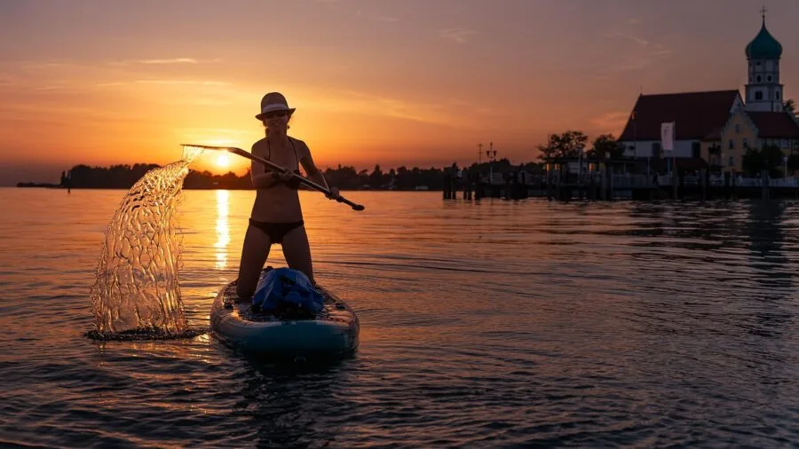 Person paddleboarding on a calm lake with mountains in the background during daytime