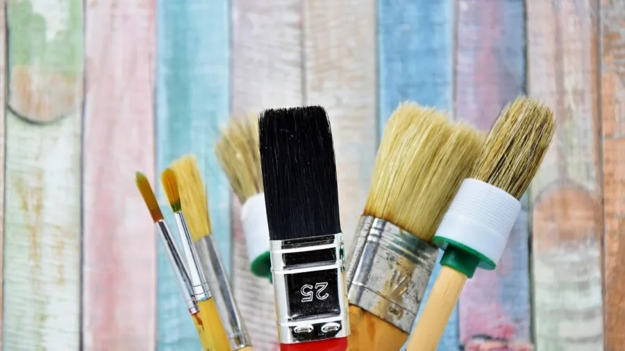 Person painting a wall with a flat brush, demonstrating even paint application on a wide surface