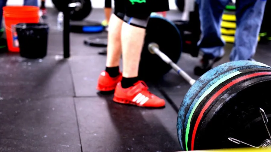 Person performing a heavy barbell squat in a gym setting, demonstrating proper form and strength training technique.