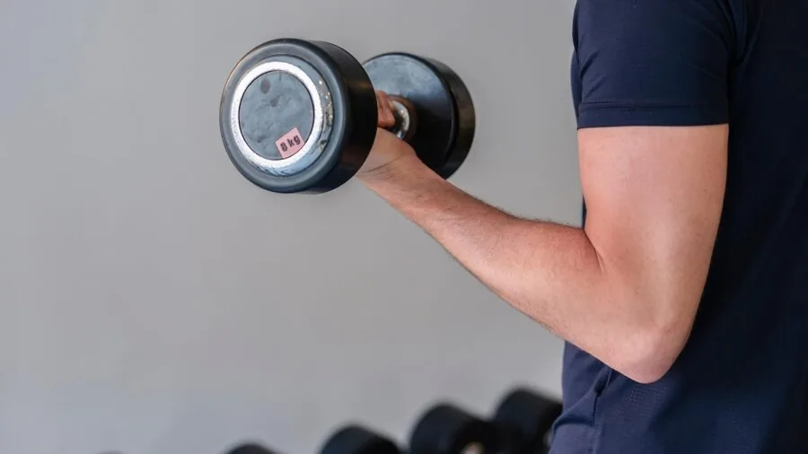 Person performing dumbbell exercise in home gym setting with fitness equipment visible