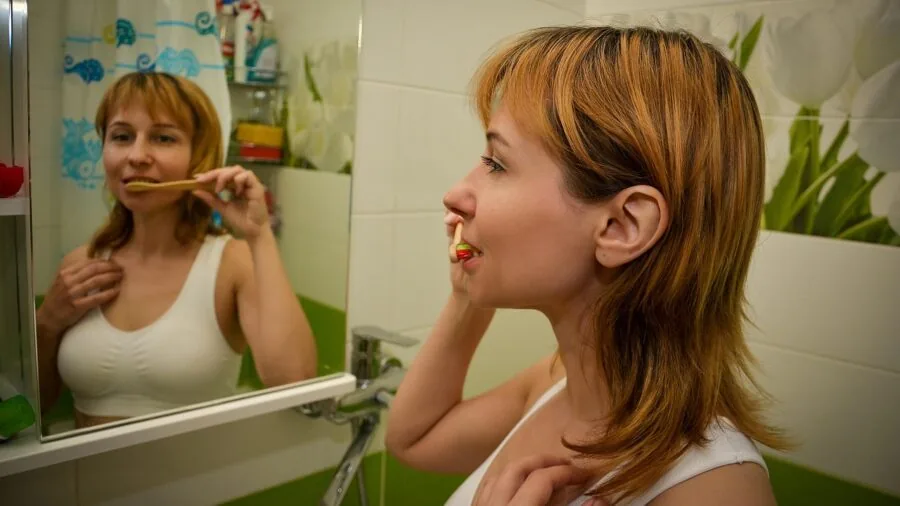 Person performing morning hygiene routine at bathroom sink with natural light