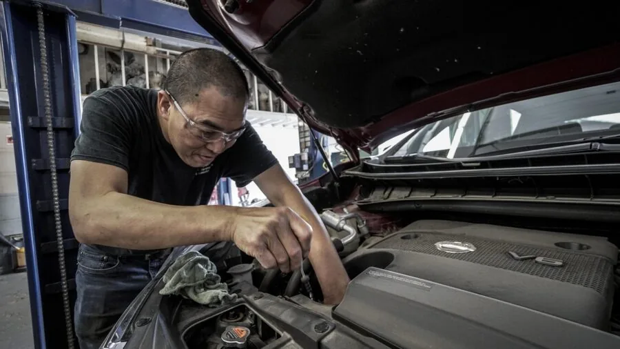 Person performing vehicle maintenance work under car hood in garage setting