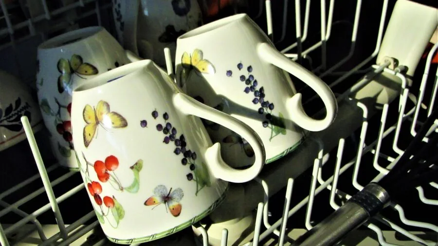 Person placing ceramic mug into dishwasher rack in modern kitchen, demonstrating dishwasher-safe cookware care