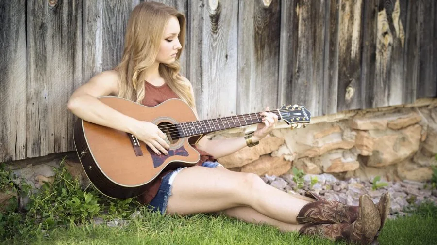 Person playing acoustic guitar in natural outdoor setting, demonstrating instrument quality and craftsmanship