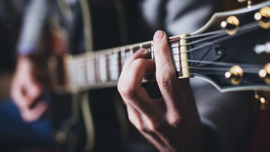 Person playing acoustic guitar outdoors in natural lighting, demonstrating strumming technique