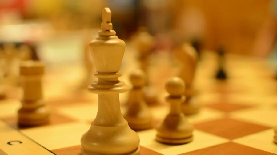 Person playing chess on wooden board, focusing on classic piece design and gameplay in natural light