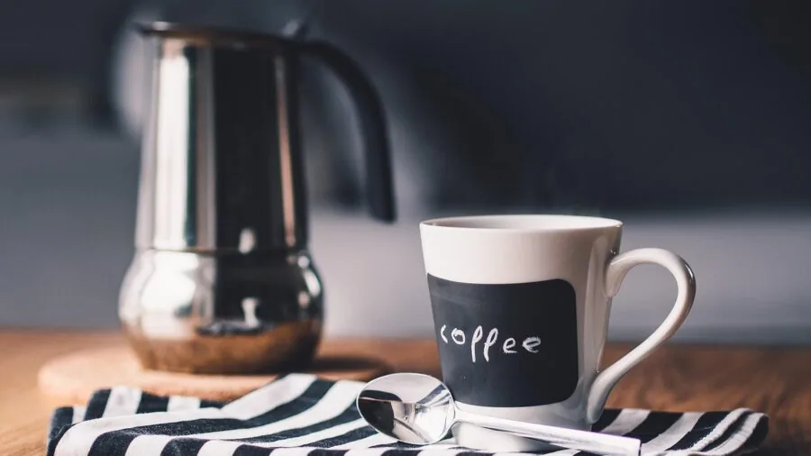 Person pouring freshly brewed coffee from glass carafe into mug in bright kitchen setting