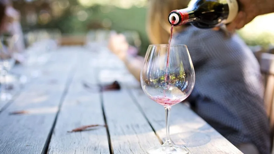 Person pouring red wine into a wide bowl glass during an intimate wine tasting moment