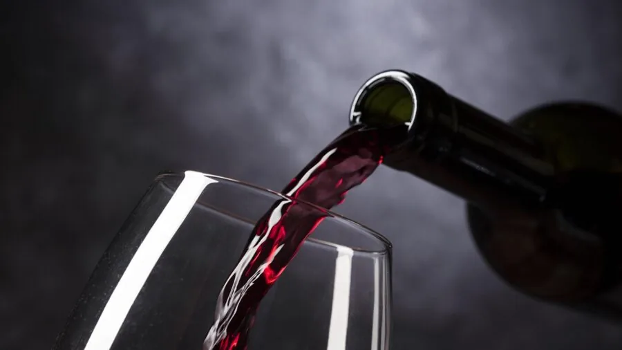 Person pouring red wine into glass, showcasing wine aeration and tasting in natural light