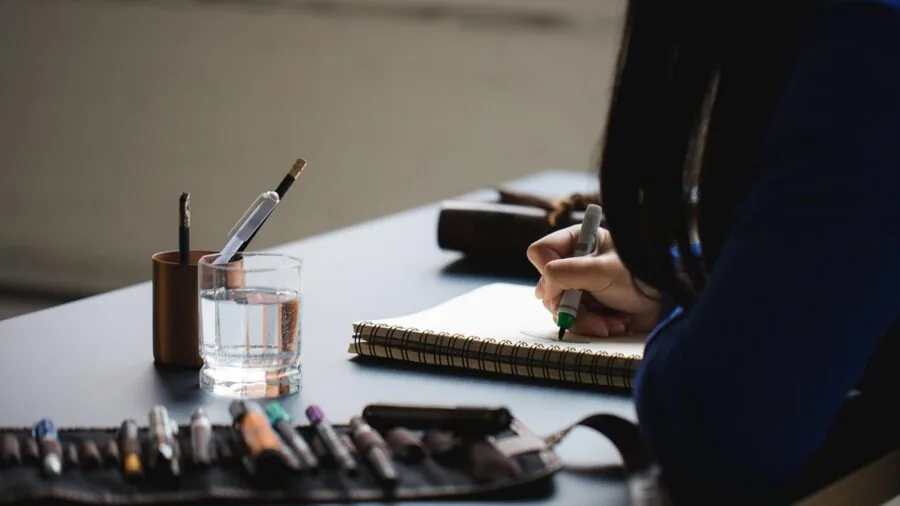 Person practicing calligraphy with pen on paper, focusing on detailed writing technique and artistic skill development