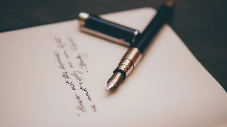 Person practicing calligraphy with pen on quality paper at a desk in natural light