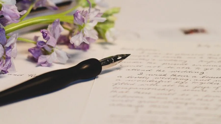 Person practicing calligraphy with various pen styles at a wooden desk with paper and ink